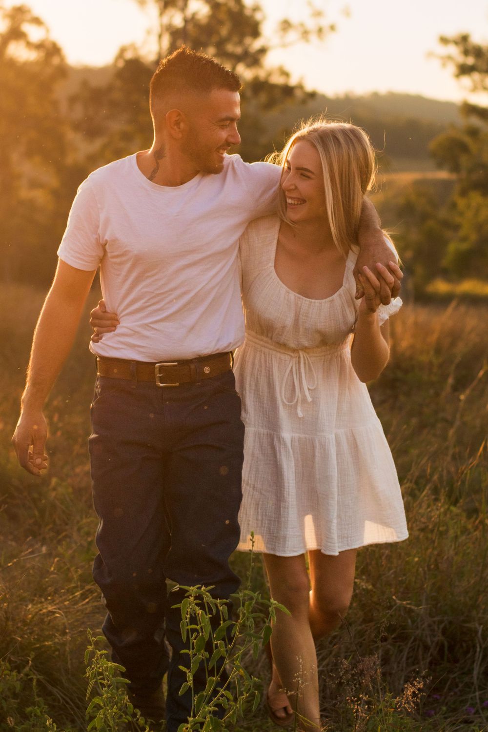 Happy couple walking together through tall grass during golden hour sunset.