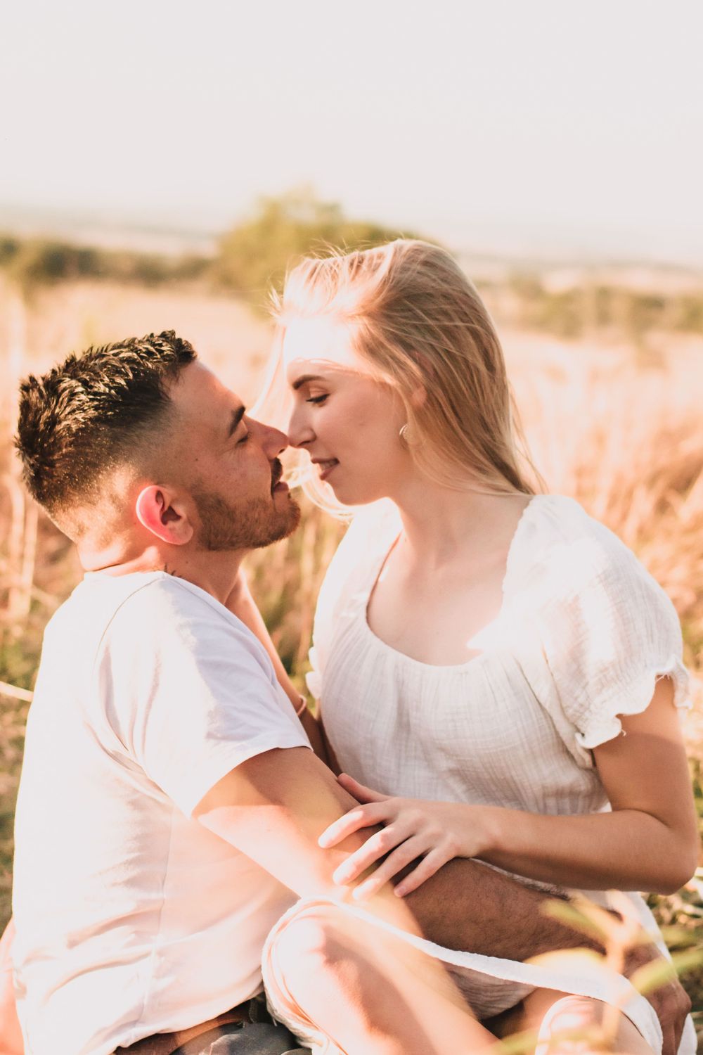 Intimate moment shared between couple in sunlit meadow during golden hour.