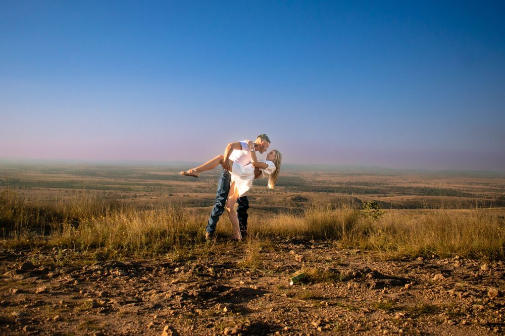 Playful couple dancing and twirling on a hilltop with expansive plains view at dusk.