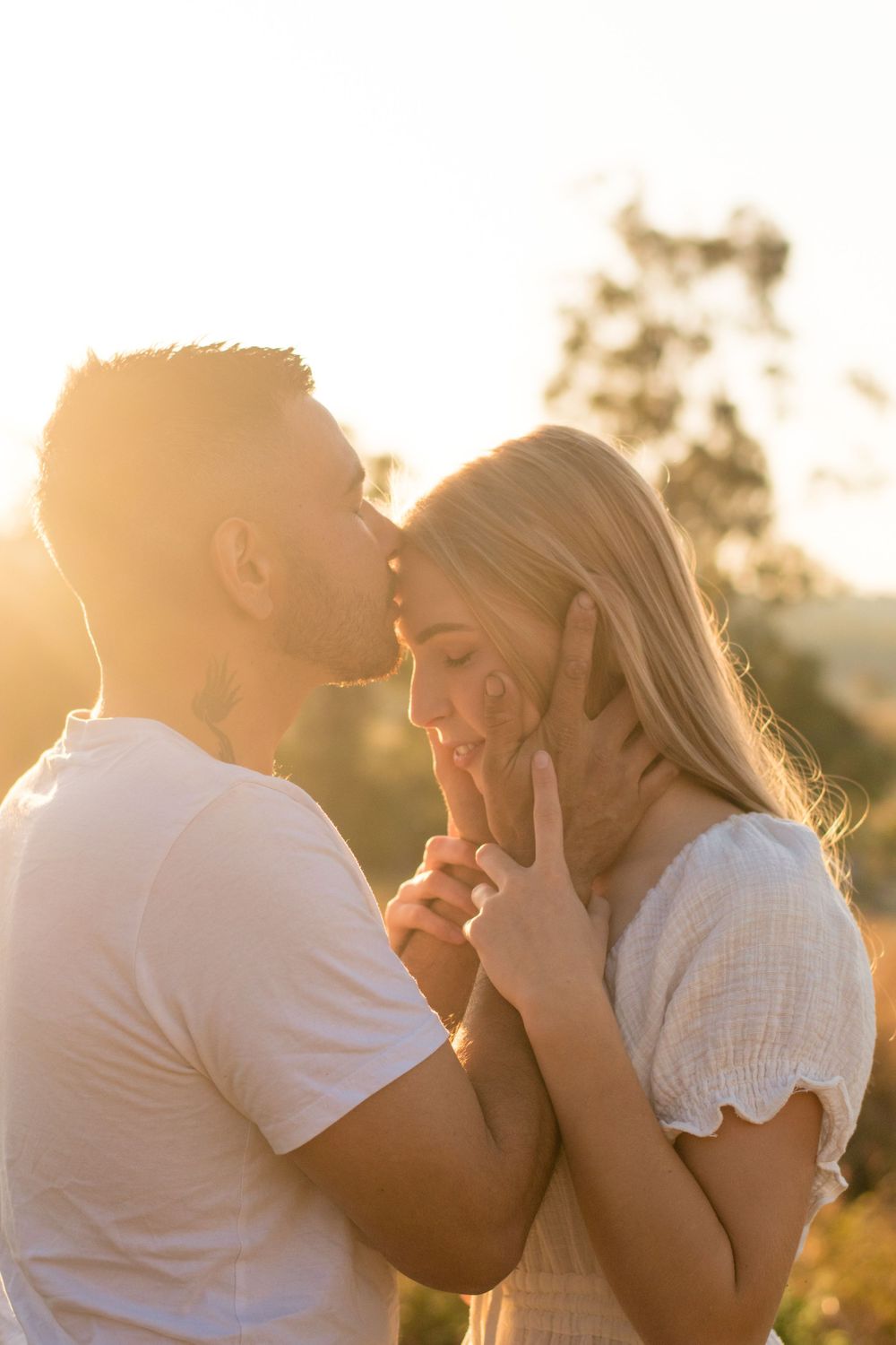 Romantic couple sharing an intimate moment during golden hour sunset in a rural field.