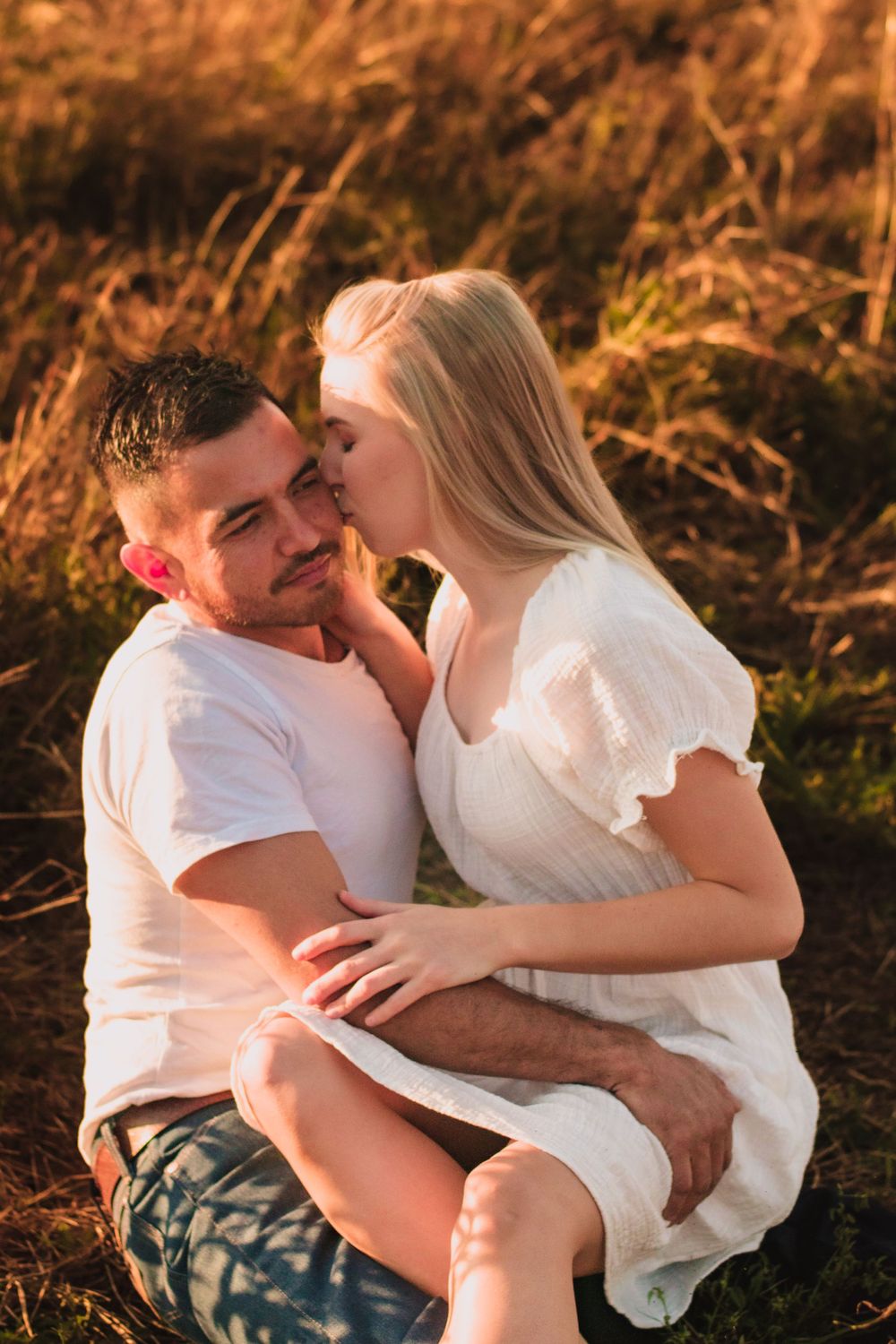 Tender moment between couple sitting in sun-kissed grass during sunset.