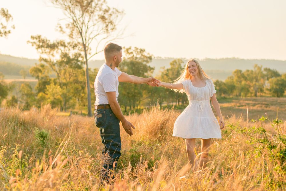 Couple holding hands in golden meadow during sunset with mountains in background.