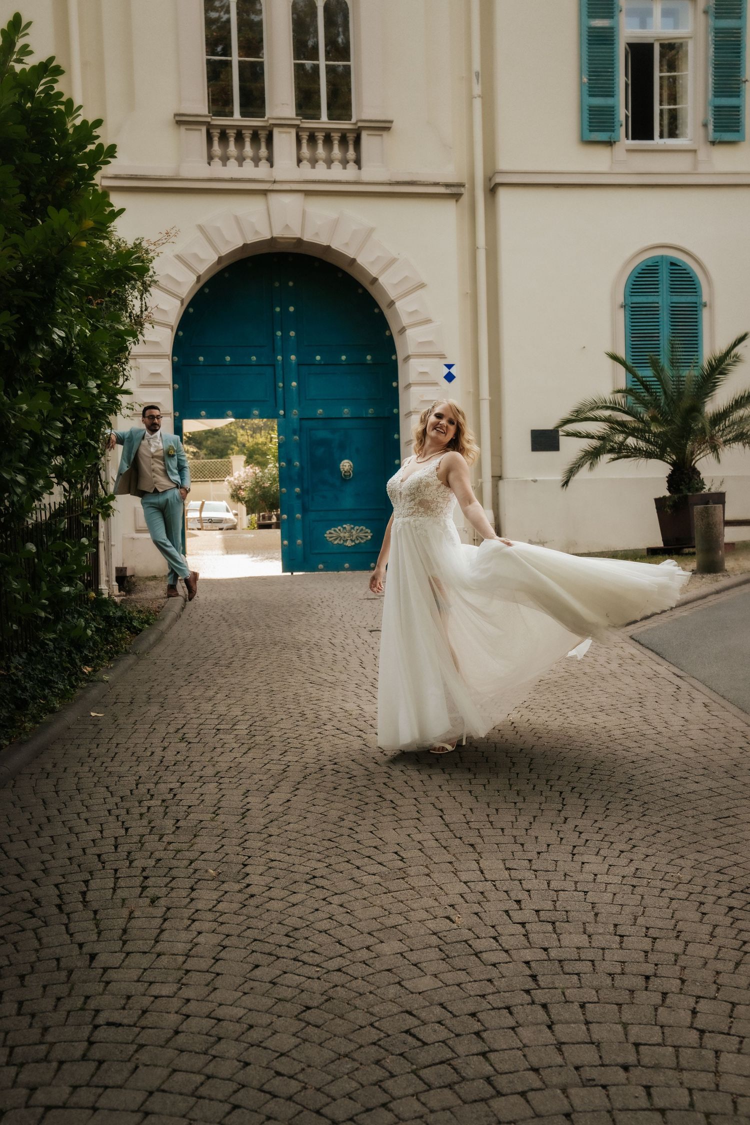Bride twirling in flowing white dress in front of blue Mediterranean door.