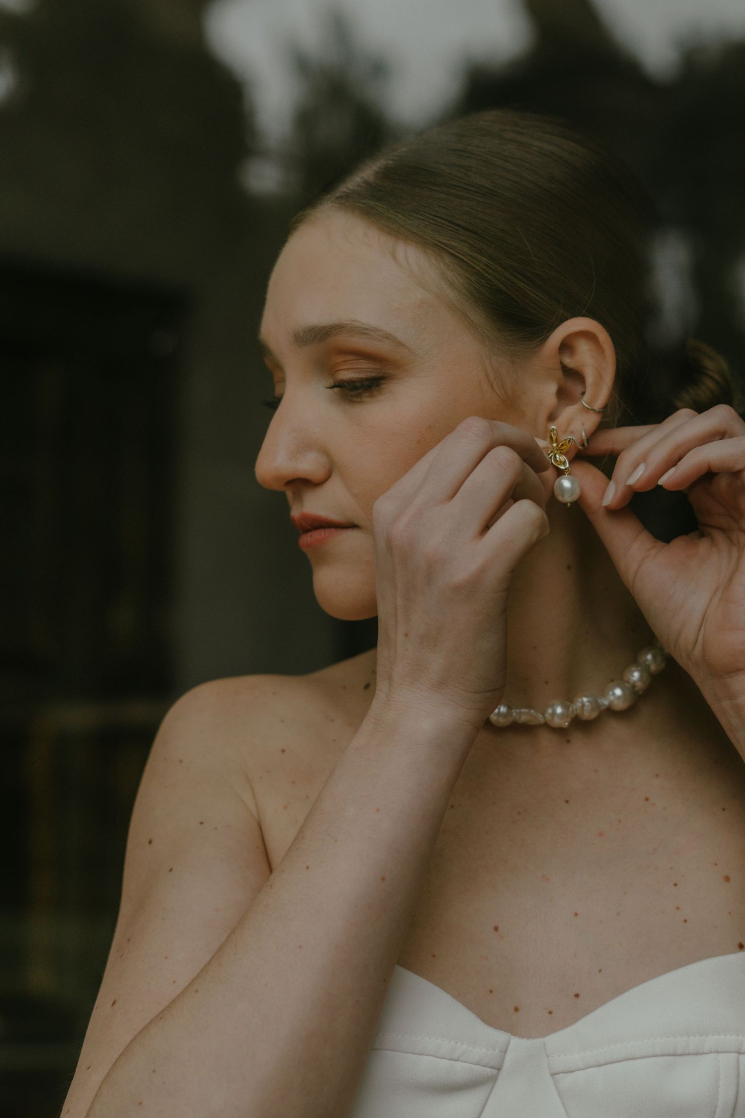A bride putting on pearl earrings in a soft, warm-toned portrait.