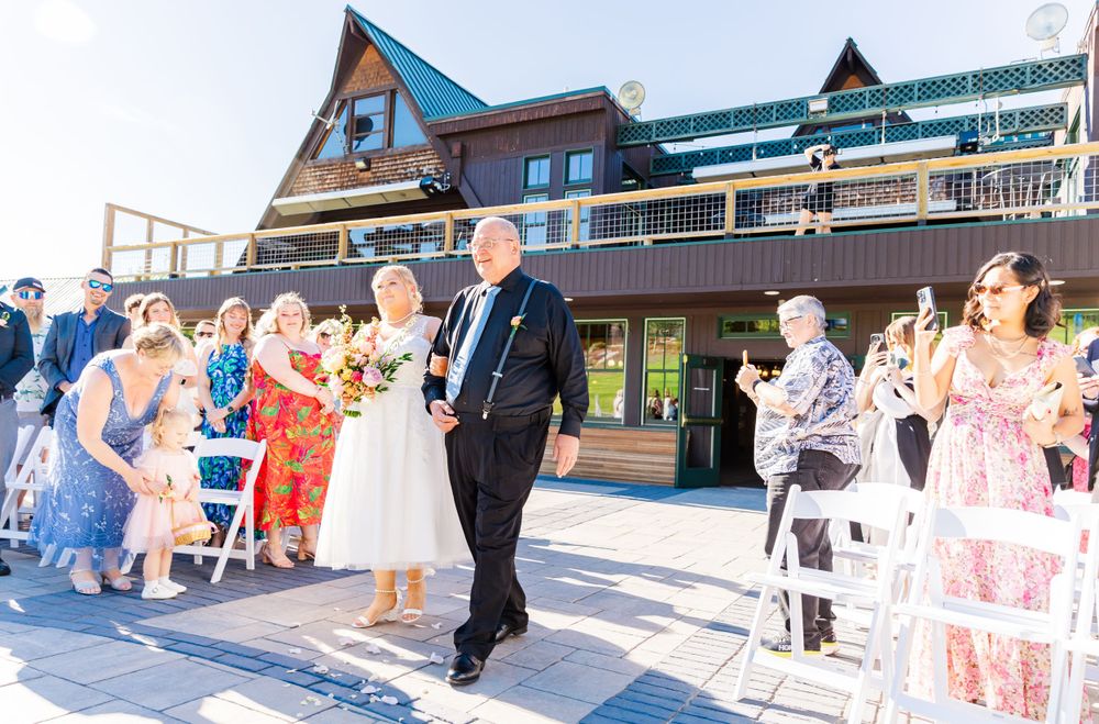 Wedding guests watch ceremony at mountain resort lodge on sunny summer day.
