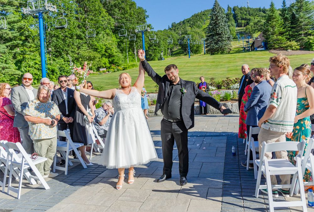 Newlyweds celebrate with raised arms during recessional at mountain resort wedding.