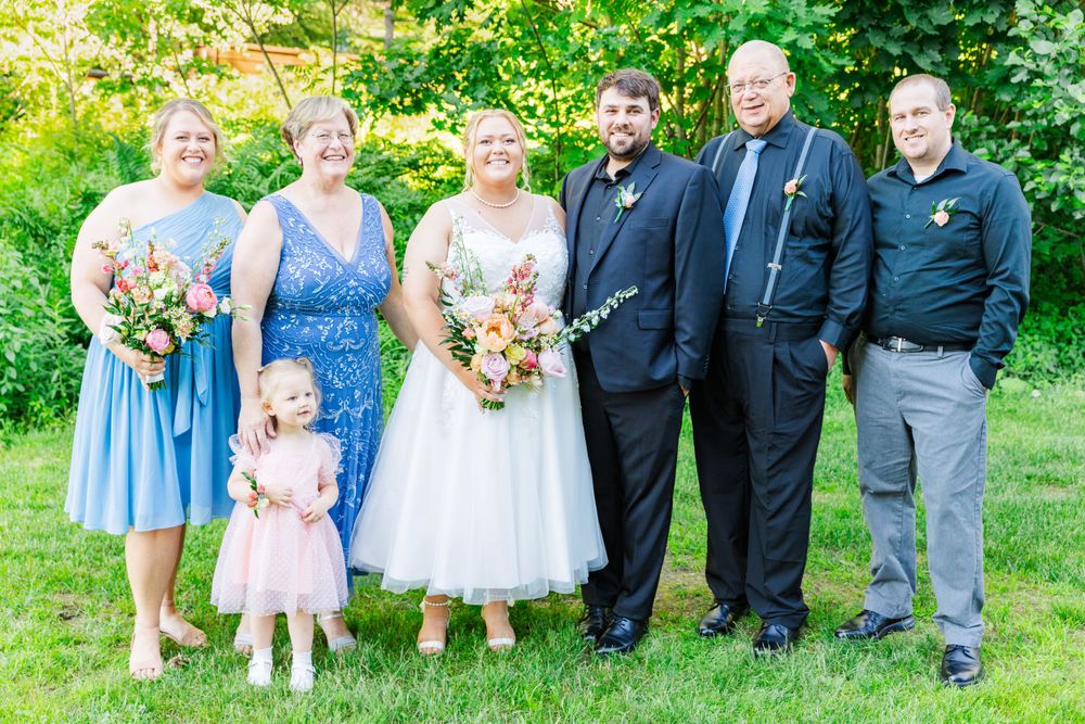 Wedding party poses for formal group photo in garden with colorful summer bouquets.