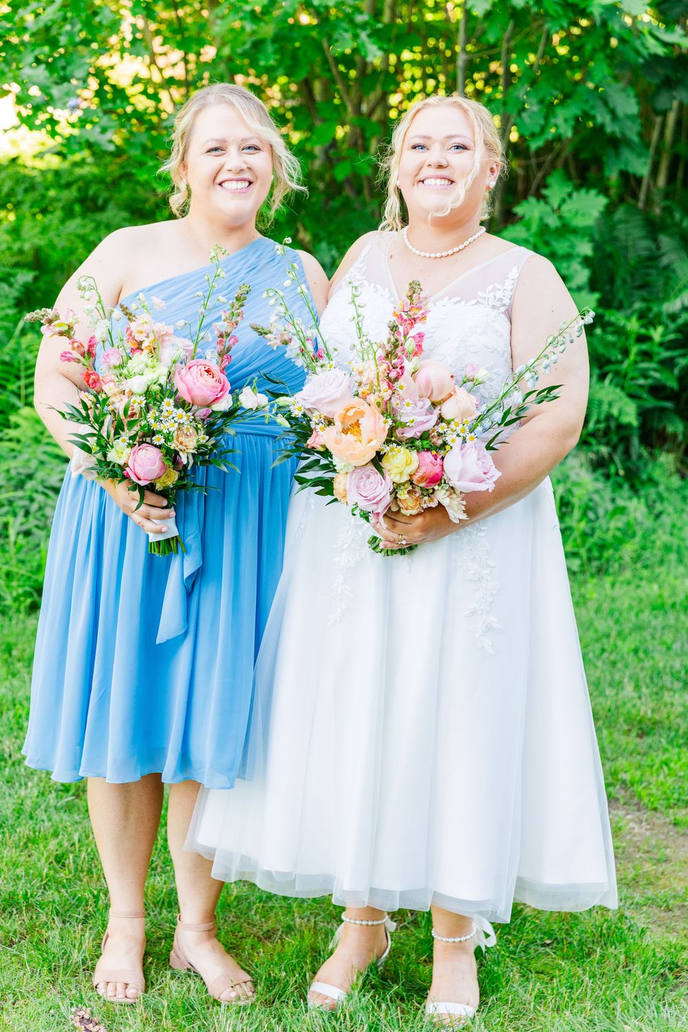 Wedding attendees in blue and white dresses hold matching bouquets of pink and peach flowers.