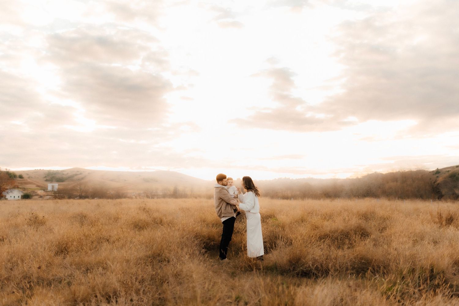 A couple standing together in a golden field at sunset.