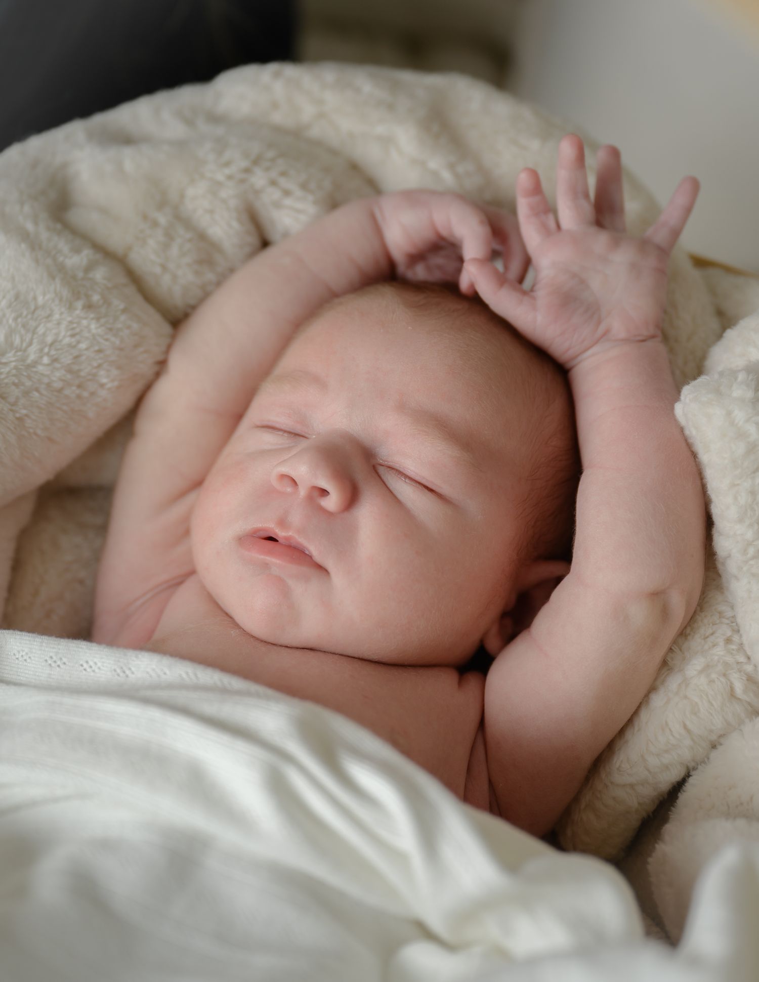 Peaceful sleeping baby stretching arms above head on soft white blanket.