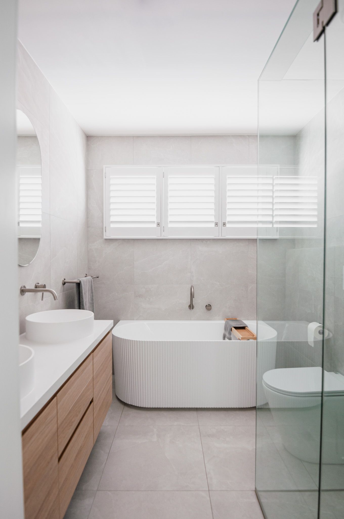 Modern bathroom featuring white ribbed bathtub, wooden vanity, and glass shower enclosure.