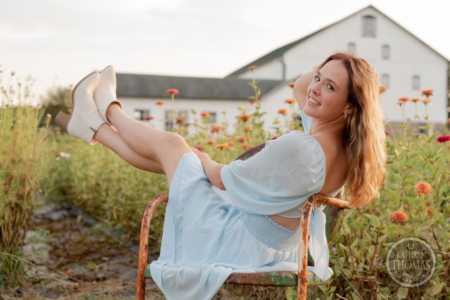 A carefree moment captured in a garden chair with a white barn and flowers in the background.