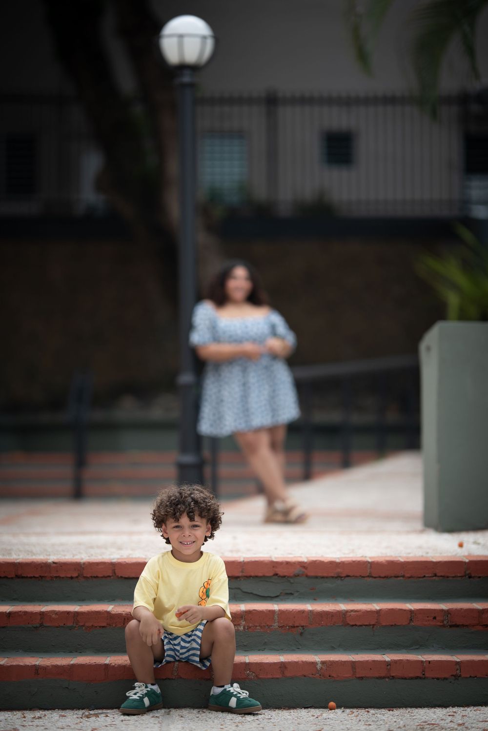 A child in yellow shirt sits on brick steps with urban background.