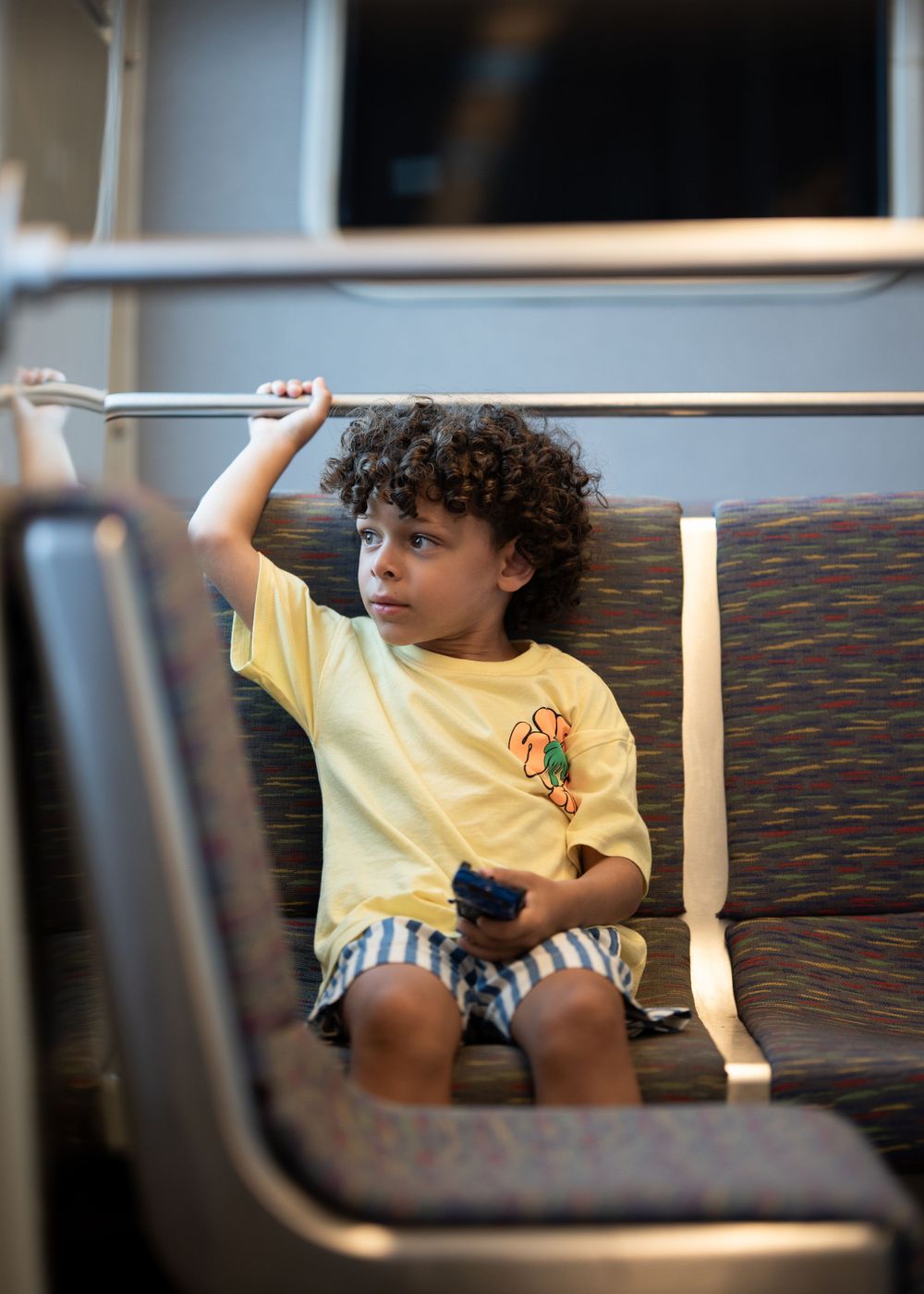Child in yellow shirt and striped shorts playing on a bench with a handrail.