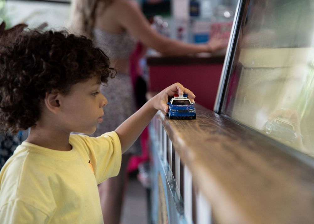 Child in yellow t-shirt playing with a toy car on a ledge.