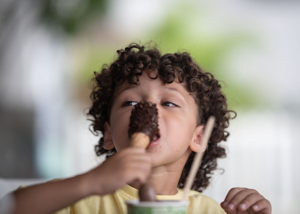 Child enjoying a chocolate ice cream cone in a yellow shirt.