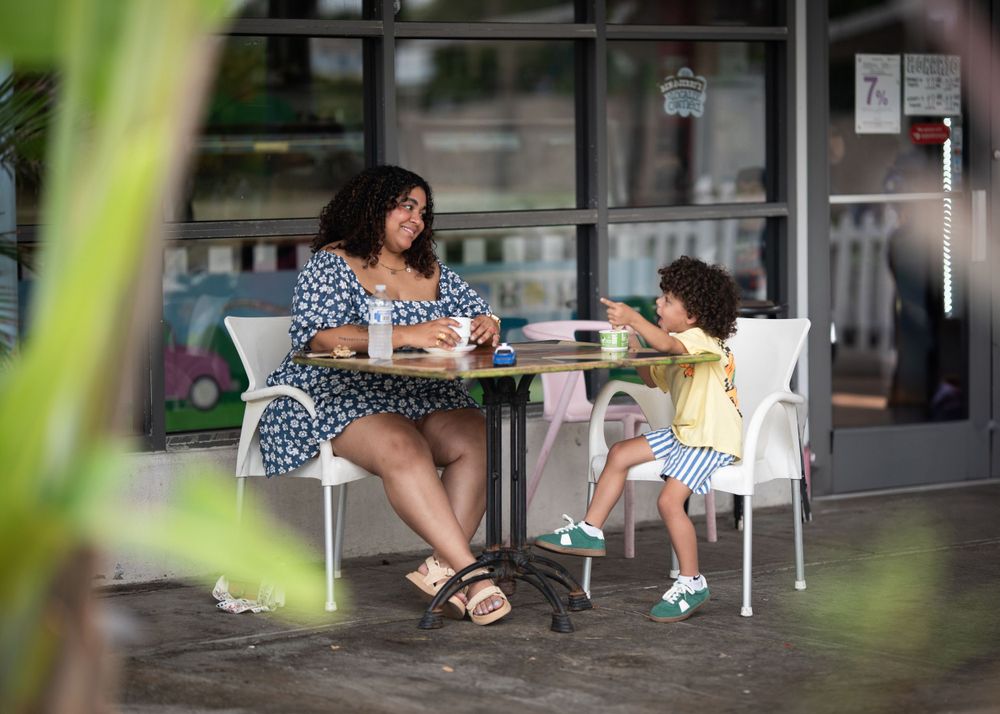 Two people sharing a moment at an outdoor cafe table framed by greenery.