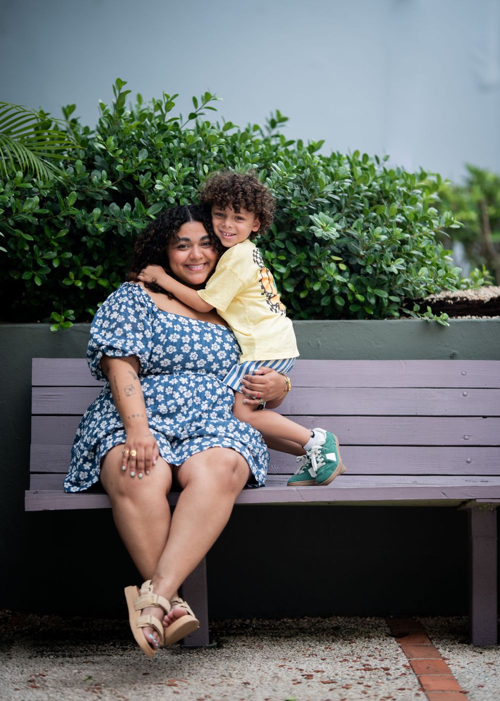 A parent and child share a tender moment on a bench surrounded by greenery.