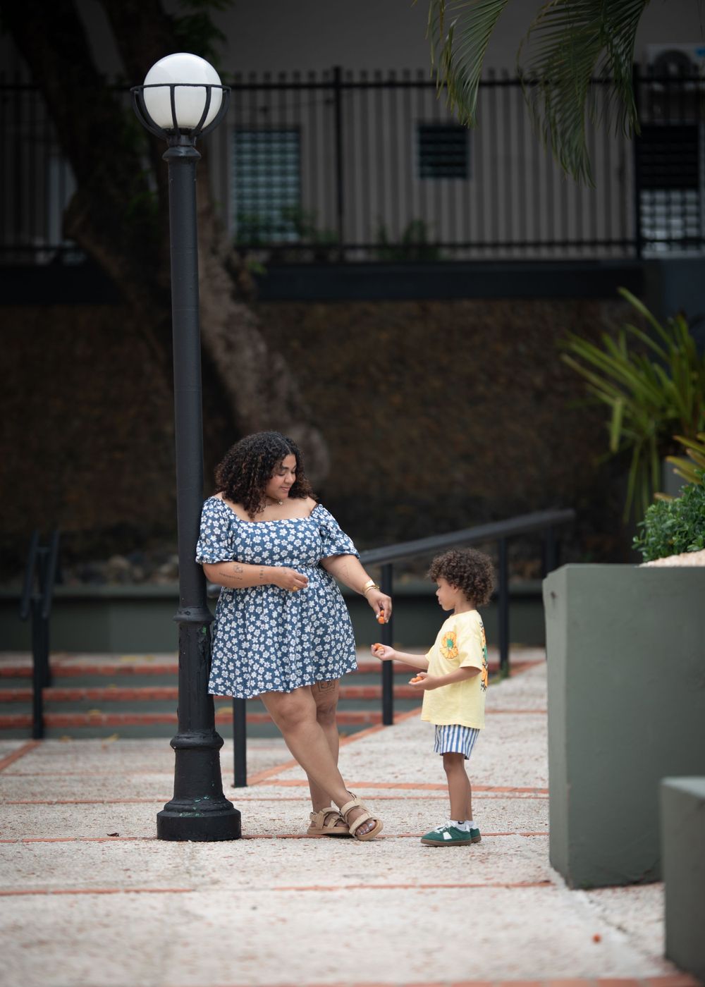 A parent and child interact playfully near a lamppost on a brick pathway.