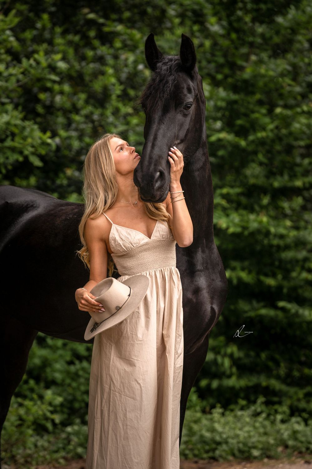 A black horse and person in a cream dress share intimate moments together in a lush outdoor setting.