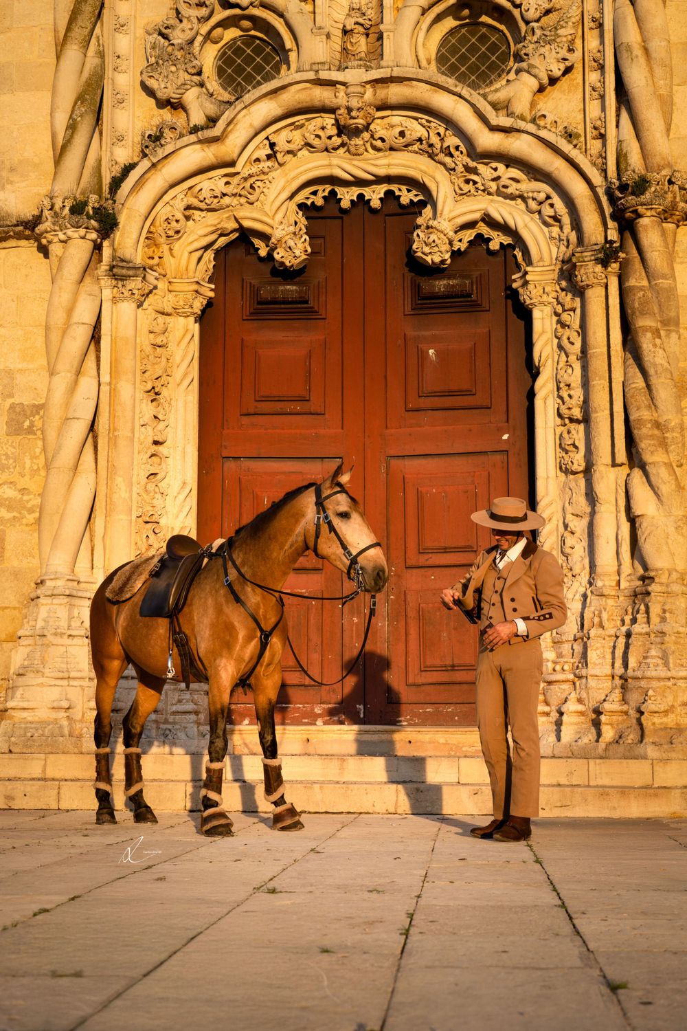 A brown saddled horse stands with its owner outside an ornate church entrance with a large wooden door.