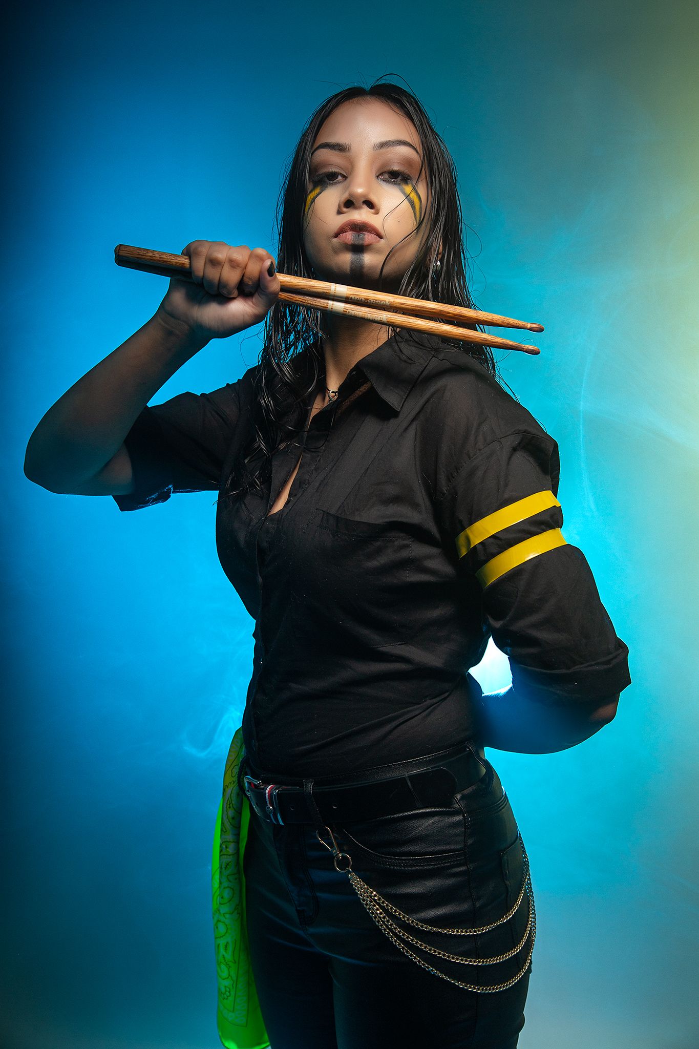 Figure in black attire holds drumsticks against blue background with dramatic lighting effect.