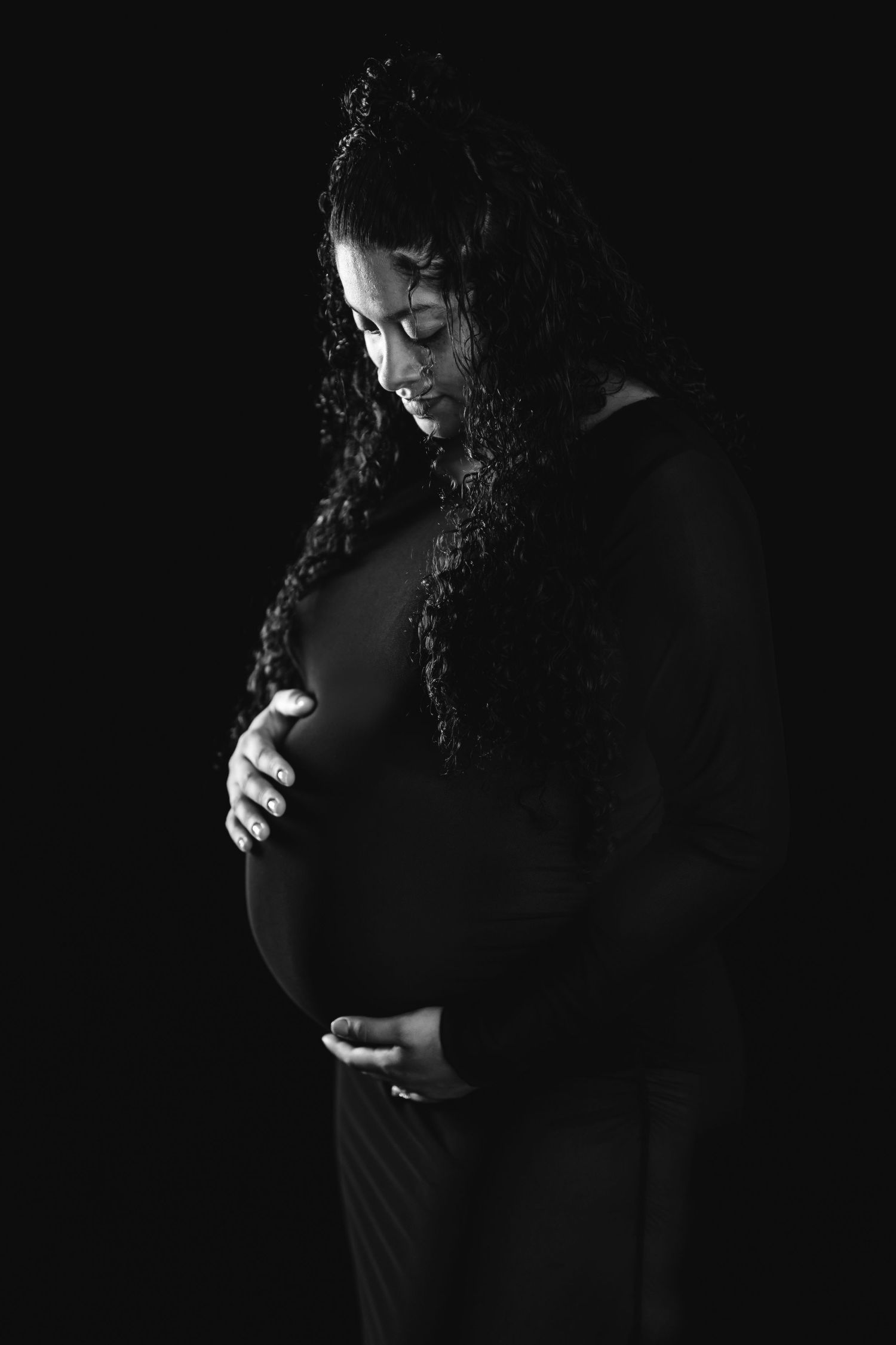 Artistic black and white maternity silhouette shows an expectant mother gently cradling her belly against dark background.  Middle Tennessee