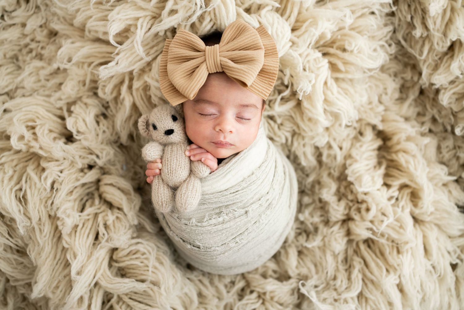 Peaceful sleeping newborn wrapped in mint green swaddle on floral background.