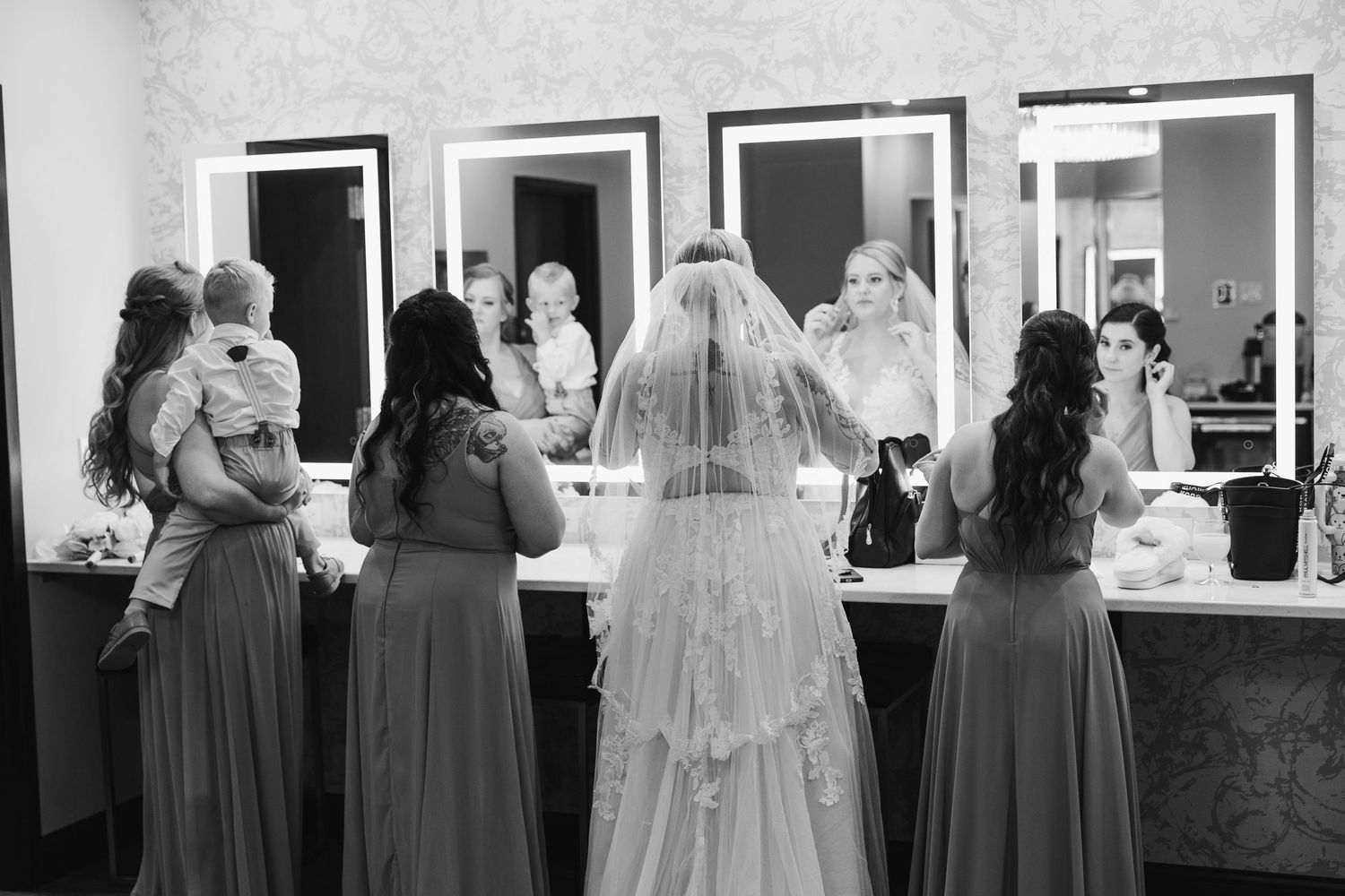 Black and white photo of bridal party getting ready in dressing room with mirrors.