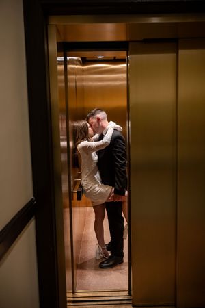 A couple sharing an intimate moment inside a dimly lit elevator with brass interior panels.