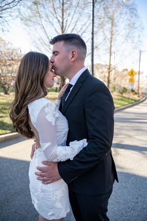 Romantic wedding photo of couple embracing on a paved road with bare trees in the background.