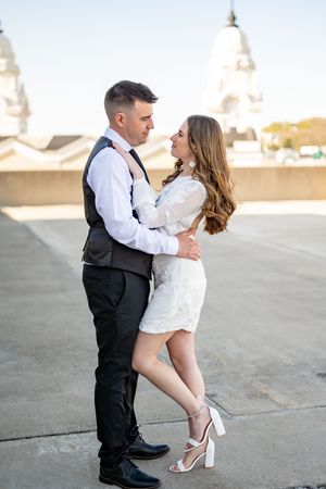 Couple embraces romantically on rooftop with white domed architecture in background during sunny day.