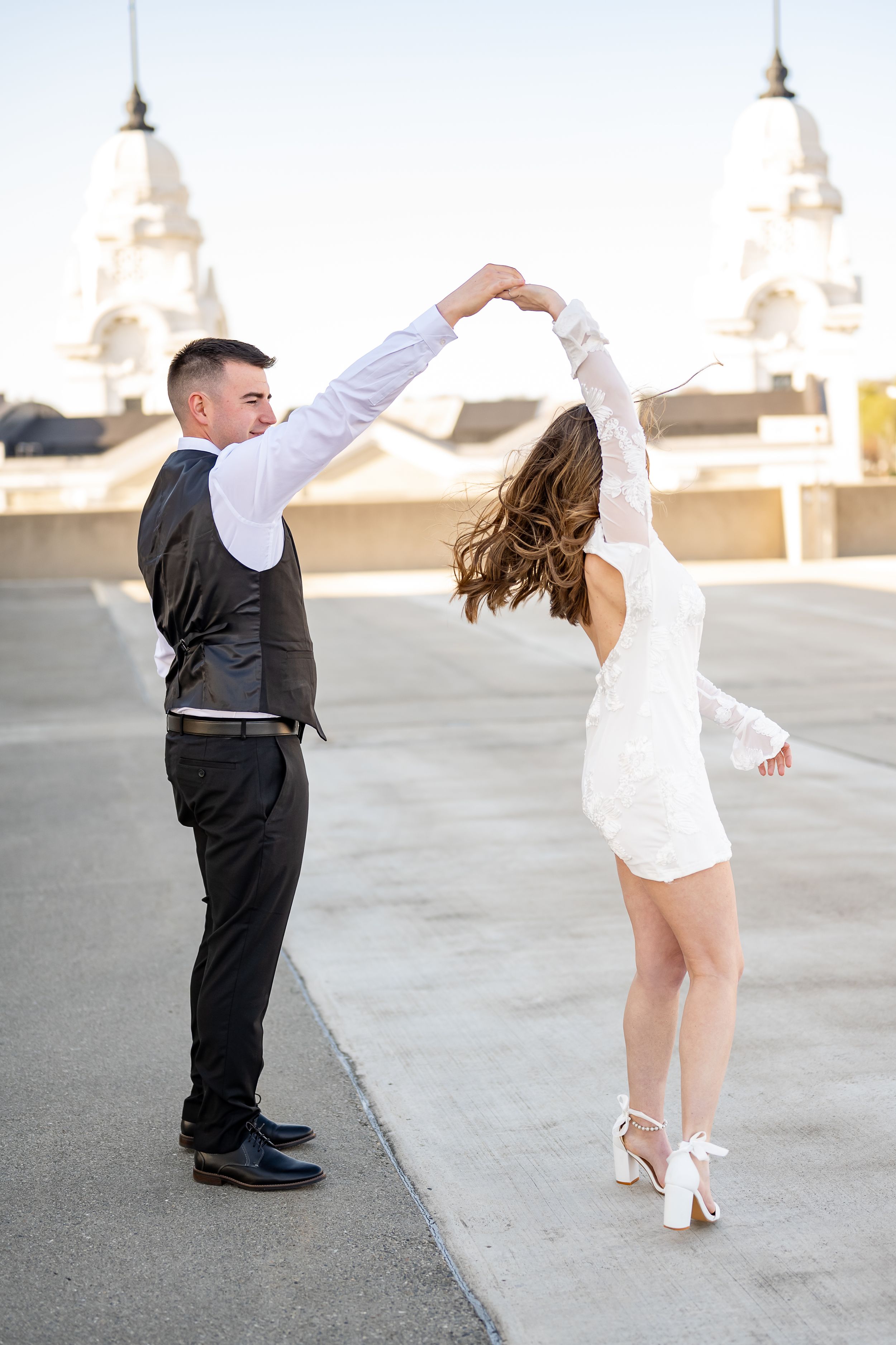 A couple dances on a rooftop with white domed buildings in the background, the woman wearing a short white dress.