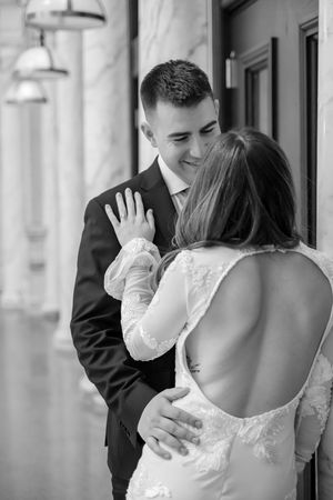 Black and white wedding photo showing intimate moment between newlyweds as bride reveals backless lace dress detail.