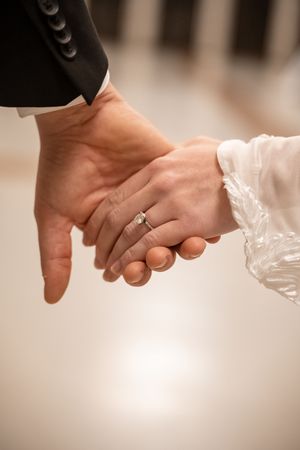 Close-up of newlywed couple holding hands with engagement ring visible on bride's hand in soft romantic lighting.