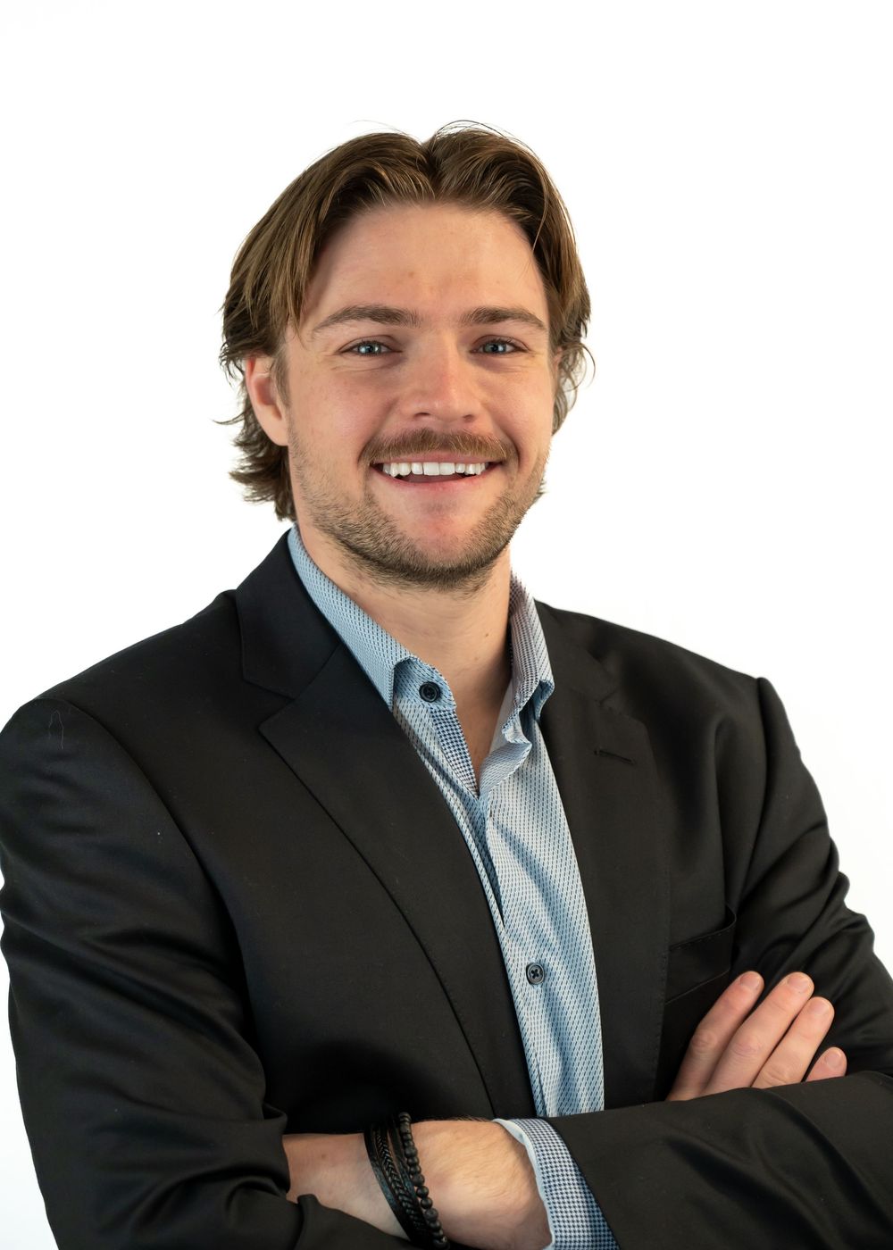 Smiling young professional man in black blazer with arms crossed against white background.