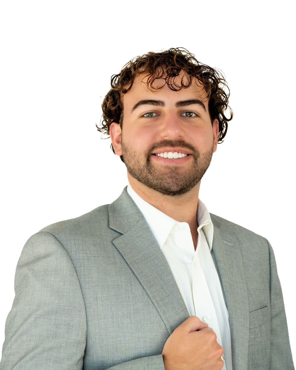 Young professional man with curly hair and beard smiling in a light gray blazer against white background.