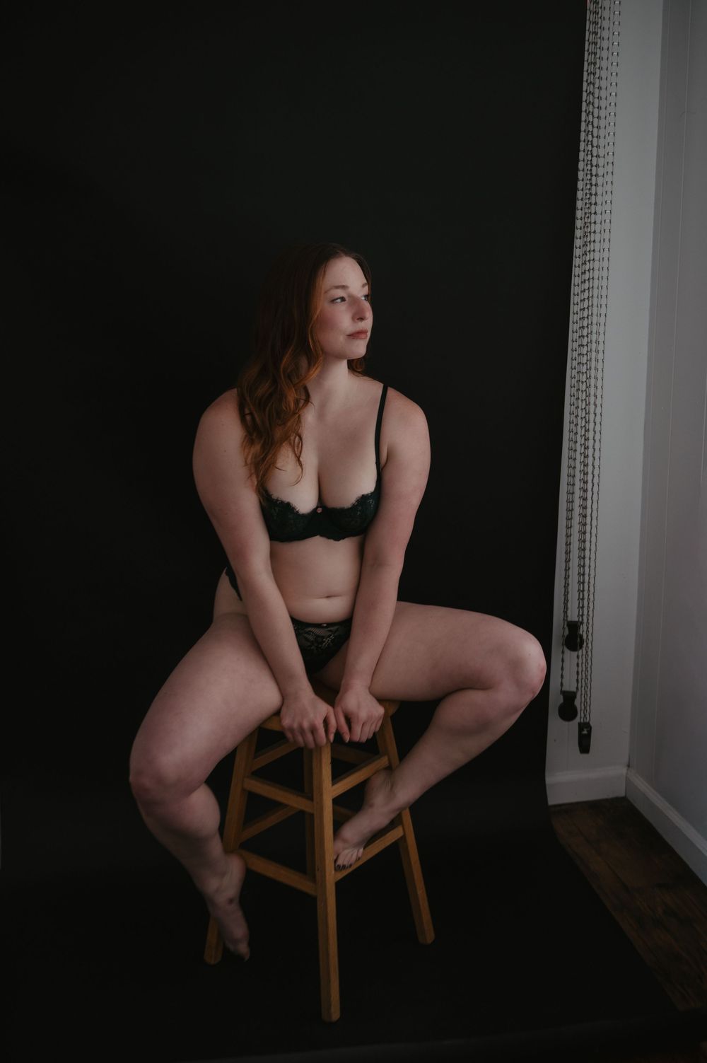 Woman sitting on chair during boudoir session with dramatic lighting