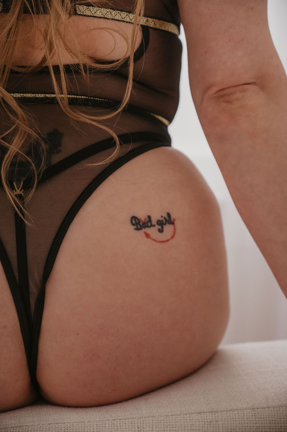 Close-up of a bad girl tattoo on upper thigh of woman wearing black sheer lingerie bodysuit.
