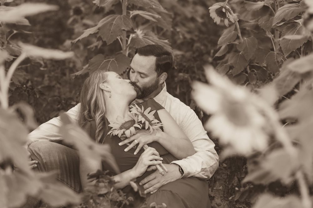 A romantic sepia-toned moment captured between two people embracing amidst foliage in a garden setting.