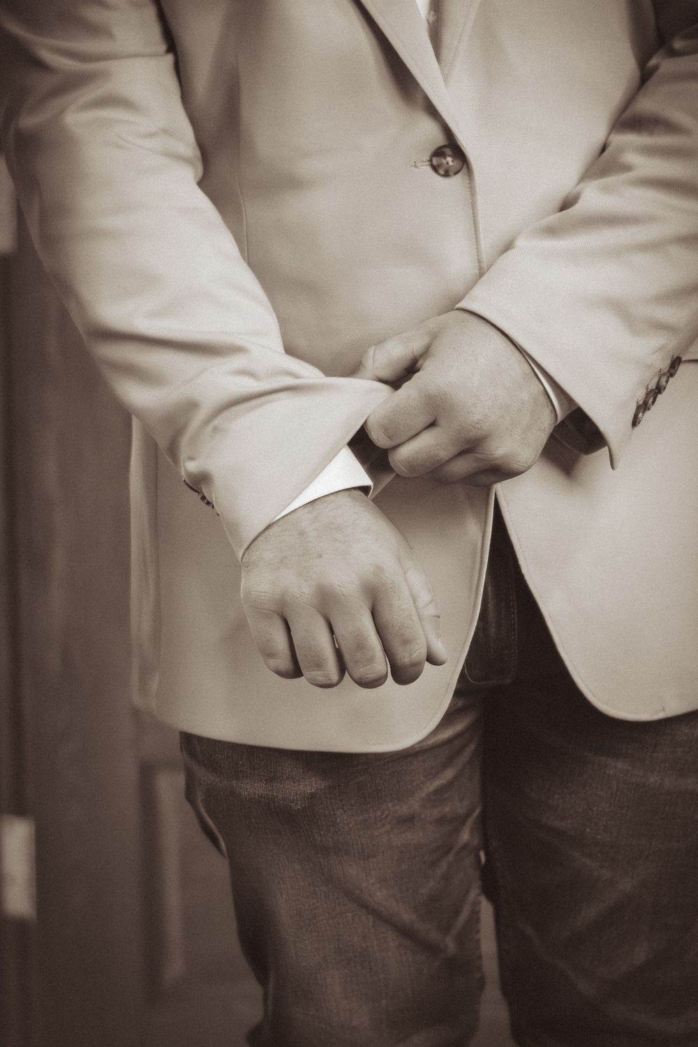 Close-up of hands adjusting the sleeve of a light-colored formal blazer.