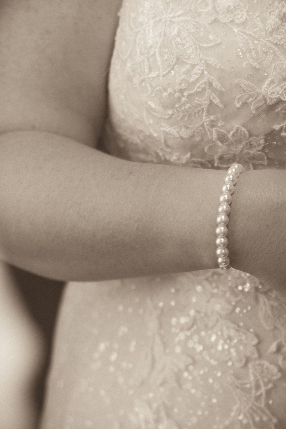 A delicate pearl bracelet worn with intricate lace wedding dress details.