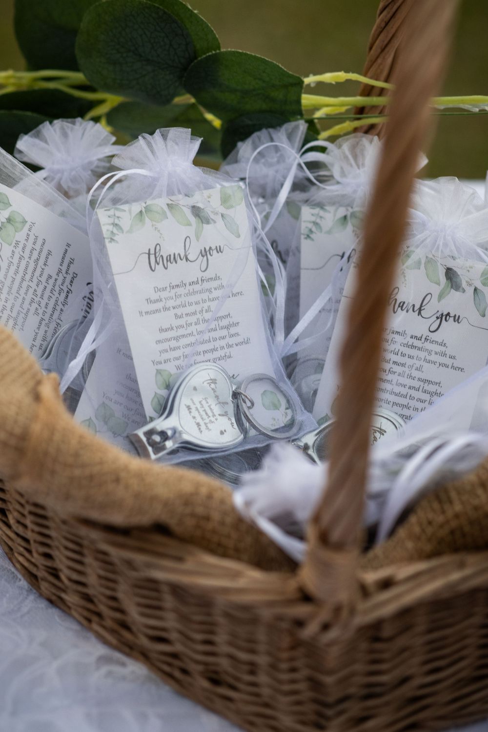 White tulle wedding favor bags with thank you notes arranged in a wicker basket.