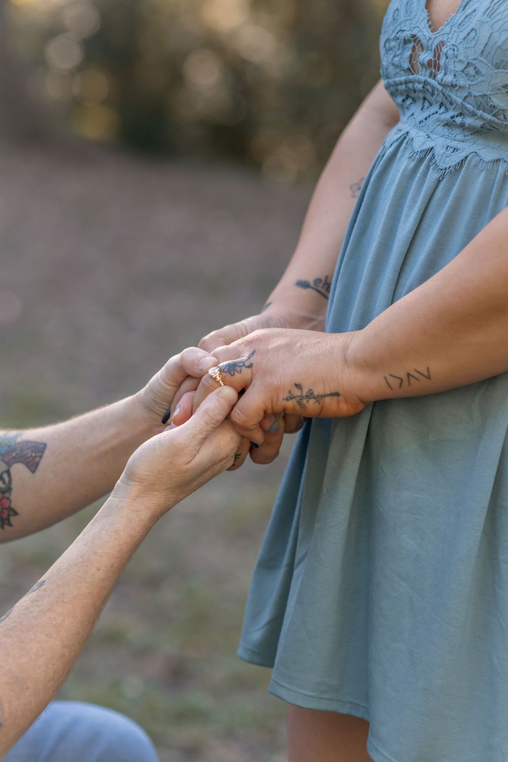 A close-up shot of hands exchanging a ring with delicate tattoo details visible.