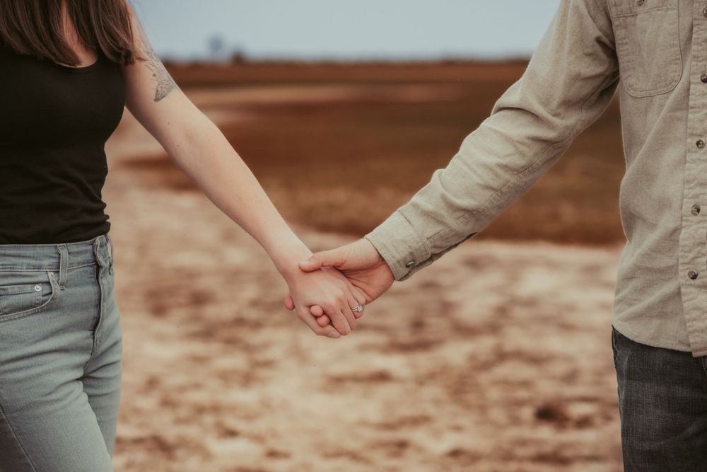 Close-up shot of couple holding hands against rustic background.