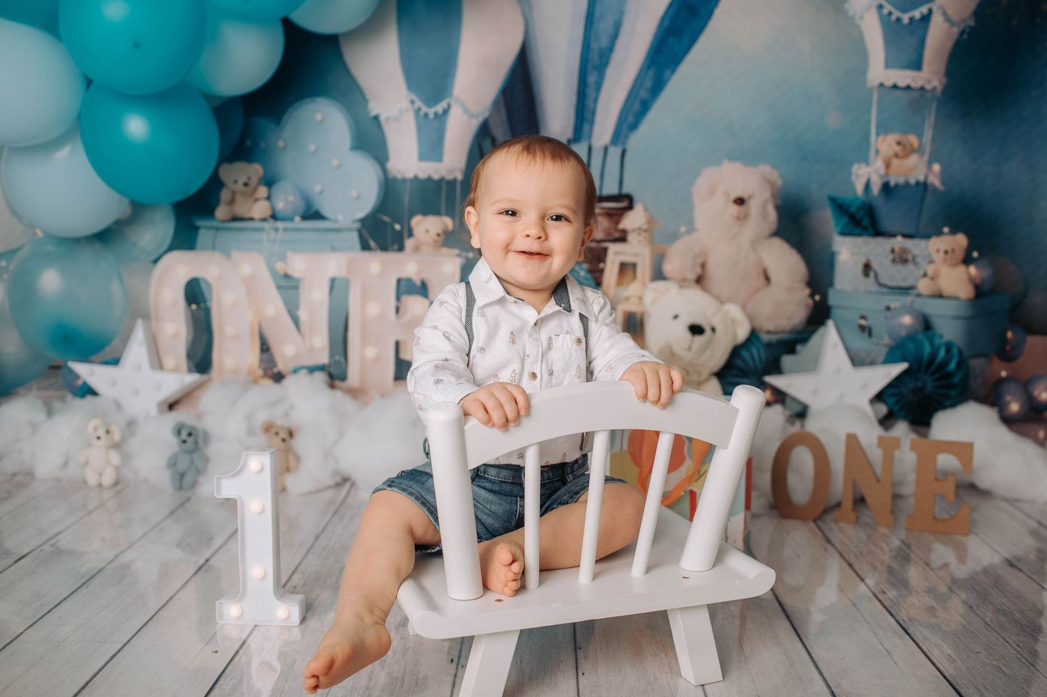 Birthday setup with white rocking chair against teal balloons and hot air balloon themed backdrop.