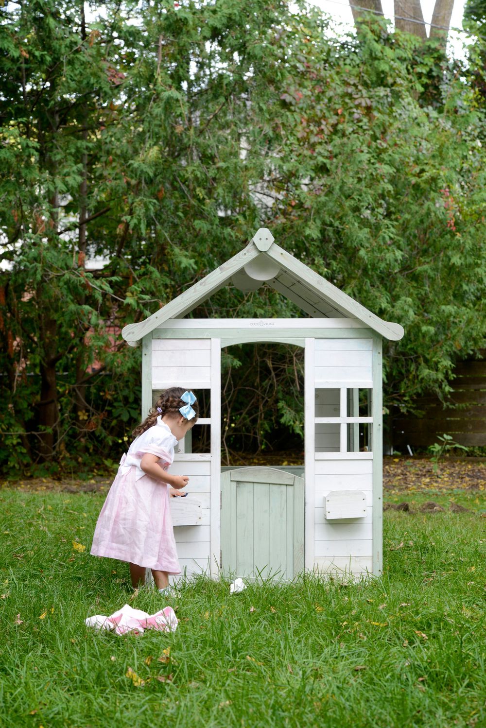 Charming white playhouse in a garden with flowering trees.