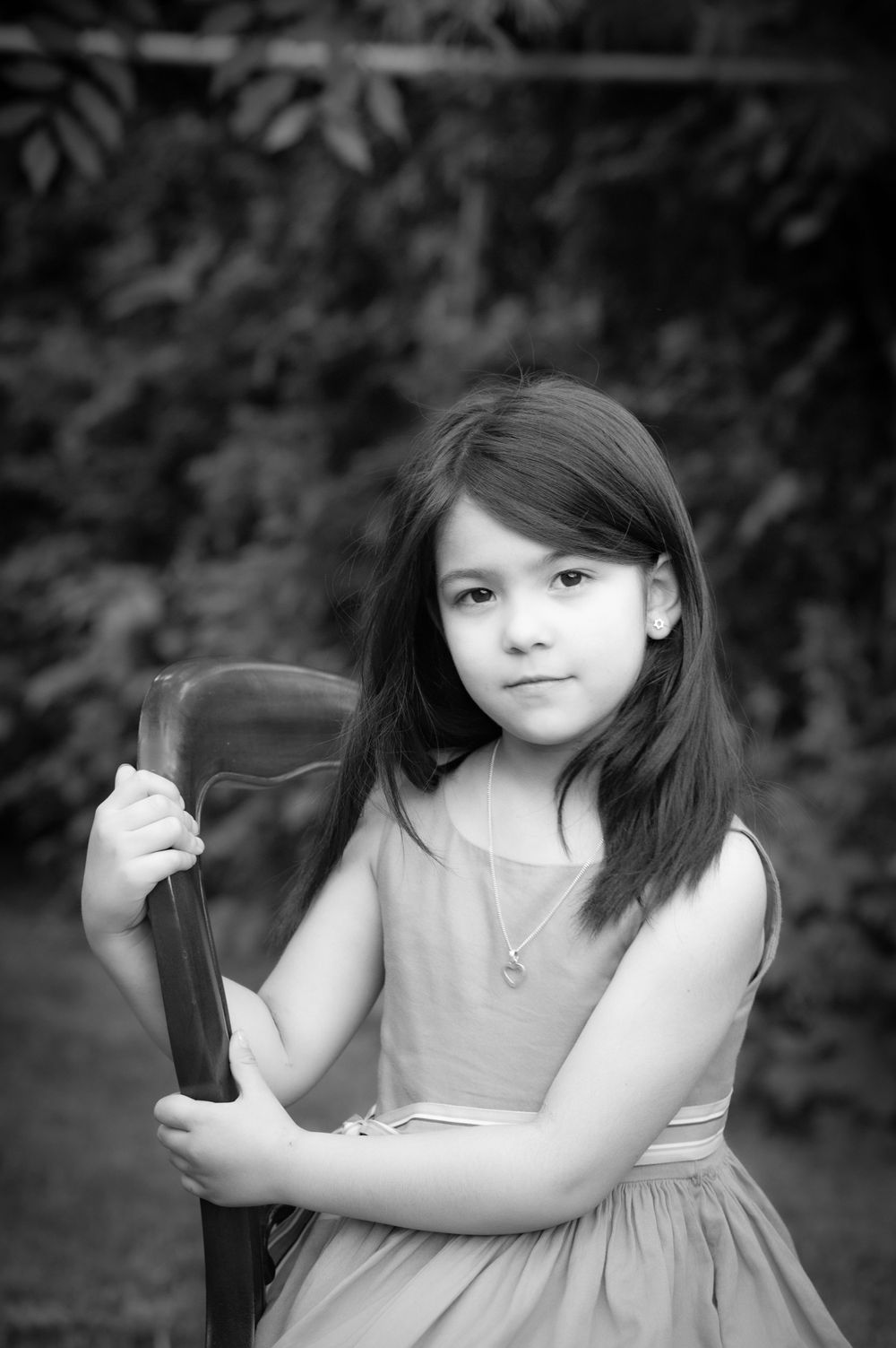 Portrait of young person in dress holding chair against blurred nature background.