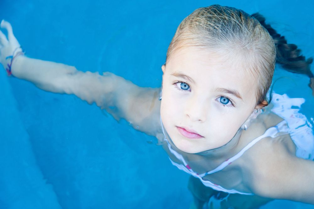 Child swimming in bright blue pool water viewed from above.