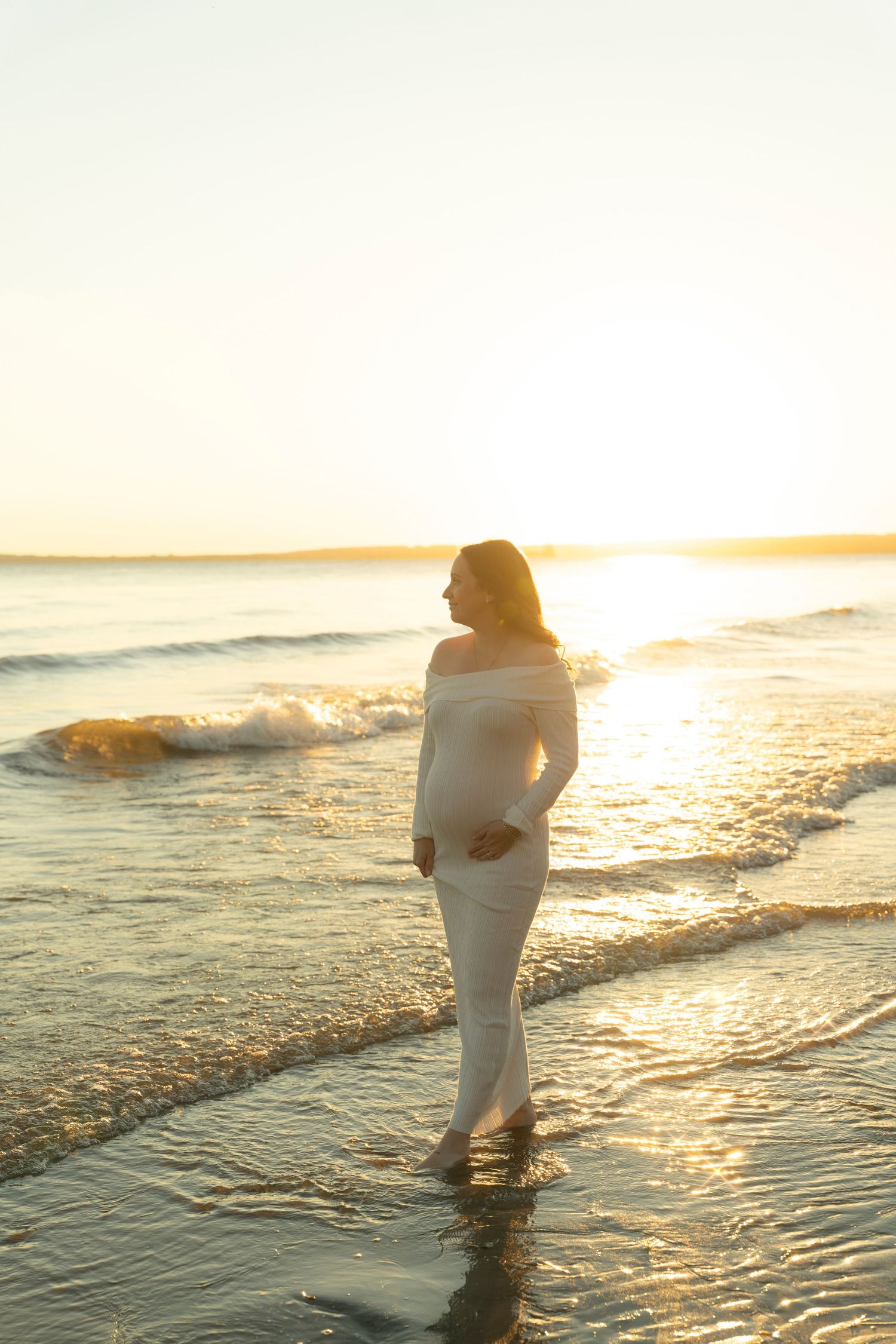 Person in white dress walking along shoreline during golden hour sunset.
